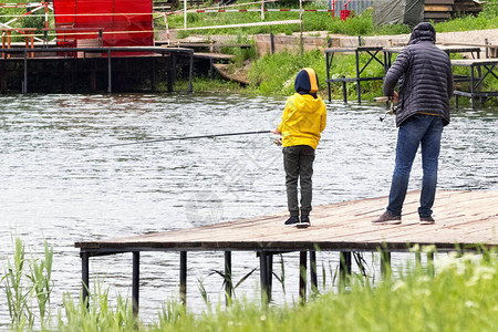 父亲教他的儿子钓鱼父亲节的概念穿着黄色夹克的图片