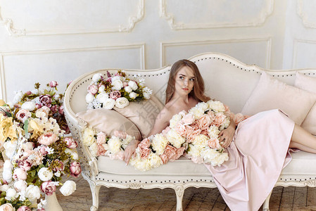 很多花朵中美丽的美女坐在浅色的沙发上美貌皮肤护理和女概念背景图片