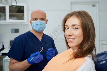 一位戴着医用面罩的秃头牙医拿着一面牙镜和牙科探查器图片