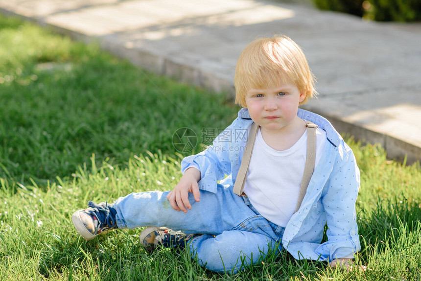 金发小男孩坐在绿草地上图片