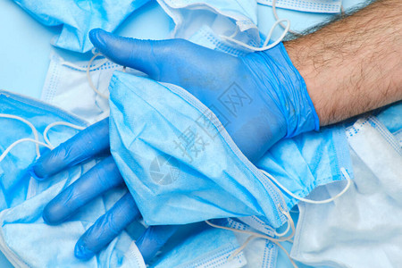 持有橡胶蓝色手套的男子用一次外科手术口罩戴在其他面罩的背景上图片