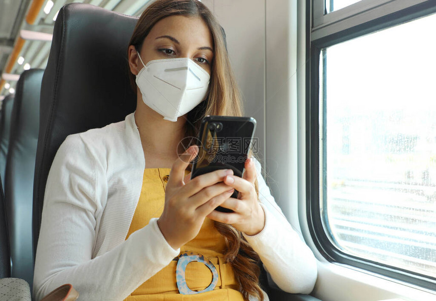 使用智能手机应用程序佩戴KN95FFP2面罩的轻松女训练戴着防护面罩旅行的乘客坐在商务舱里用手机发短信乘坐公共交通图片