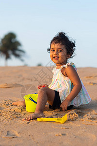 俏皮的漂亮印度女孩儿童婴儿在海滩边玩沙包并给图片