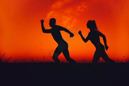 一个男人和一个女孩的轮廓冲着橙色天空跑来去高清图片