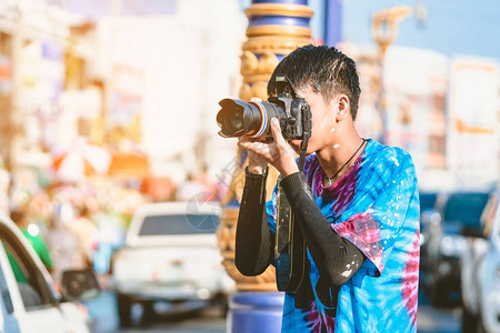 一名身着湿衣服的年轻摄影师用DSLR相机拍摄城市路上Songkran背景图片