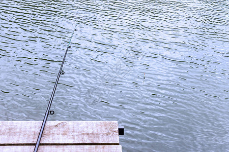 一根钓鱼竿躺在一个悬在水面上的木墩上渔夫的一天的概念夏季和秋季的图片