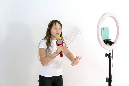 一个手里拿着麦克风的少女一边唱歌一边拍视频自拍手机安装在三脚架上背景图片