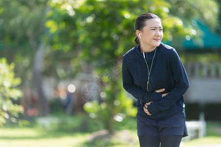 戴着耳机听音乐的亚洲女肖像在公园因胃痛而生病女人在公园锻图片