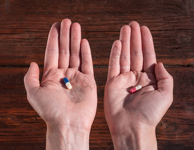 一个人手中的两片药在红色和蓝色药丸之间进行选择维生图片