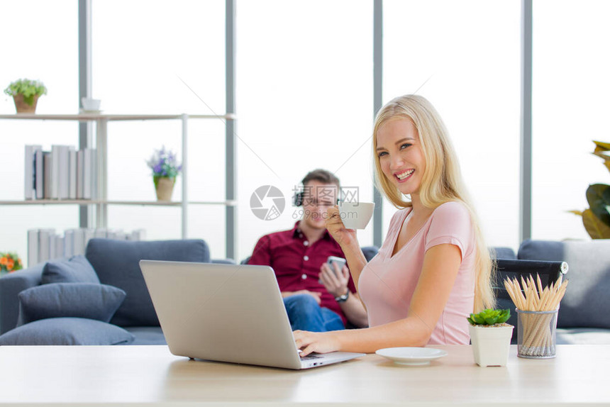 有魅力的女人在家里用笔记本电脑工作时微笑着拿咖啡杯图片
