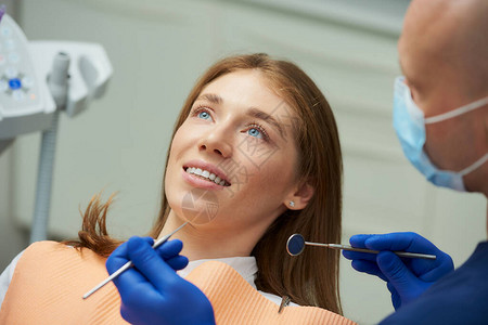 一位微笑的女士正在接受一位戴着医用面罩的男牙医和牙镜的检查图片