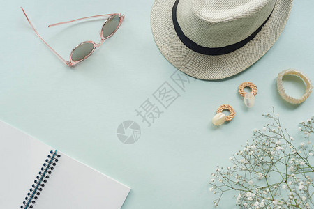 蓝色背景的太阳镜草帽耳环手镯笔记本和吉普西拉花朵图片