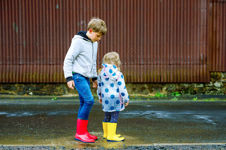 在雨夹雪中行走快乐的兄弟姐妹兄弟姐妹跳进水坑在户外玩得开心背景图片