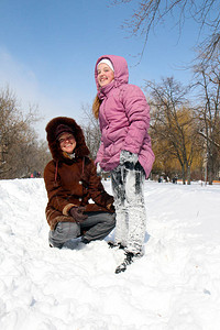 一个穿着白雪覆盖的裤子的微笑小女孩和一个微笑的年轻女子在寒冷的日子图片