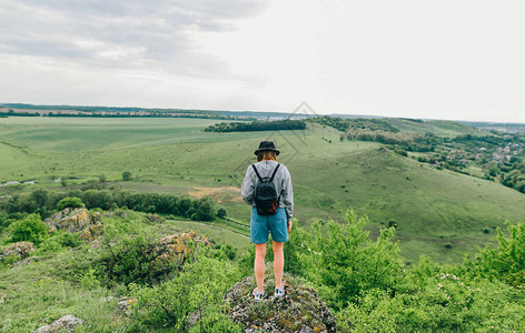 背包里的女孩徒步旅行者背对着岩石站在美丽的绿色景观背景上女游图片