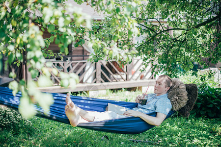 一个男人正在吊床上休息和阅读休息日和放松阳光明媚的日子里图片
