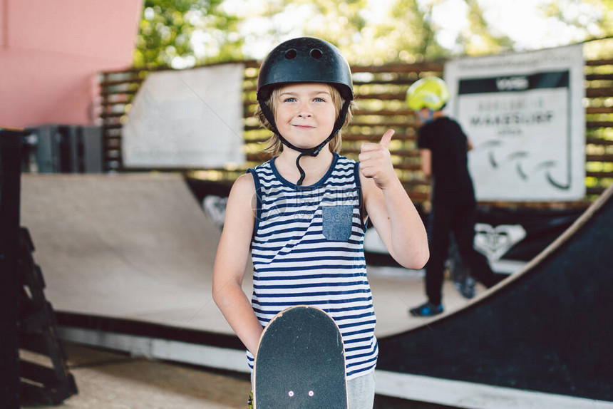 滑板男孩戴着头盔在滑板公园里摆姿势有滑板的孩子男孩童年休闲生活方式的概念肖像时尚小伙子在户外滑板主题运图片