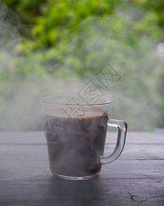一个装有热咖啡的杯子站在一扇俯瞰绿树的敞开窗户的窗台上图片