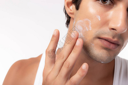 白种人年轻男子在英俊的脸上涂保湿霜乳霜或防晒霜图片