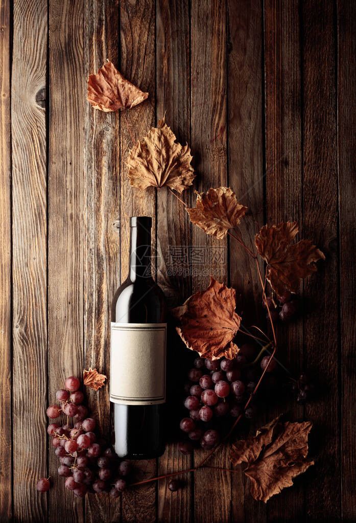 一瓶红葡萄酒与成熟的葡萄和干枯的藤叶老木背景在一个瓶子旧的空标签上复制图片