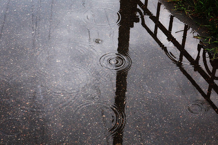 沥青上反映围栏和柱子的水坑中的雨滴水图片