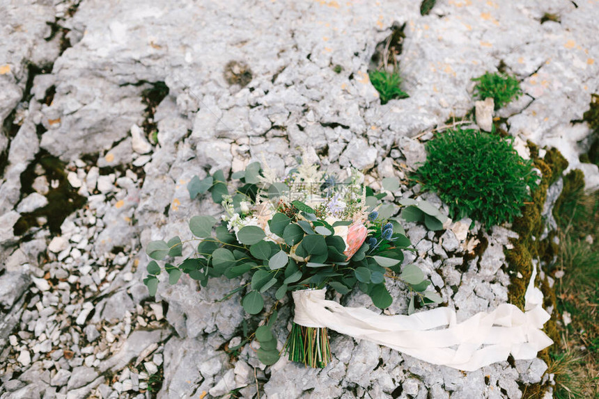 白色和奶油色玫瑰桉树枝普罗蒂亚刺飞燕草和石头上的白丝带的新娘花束图片