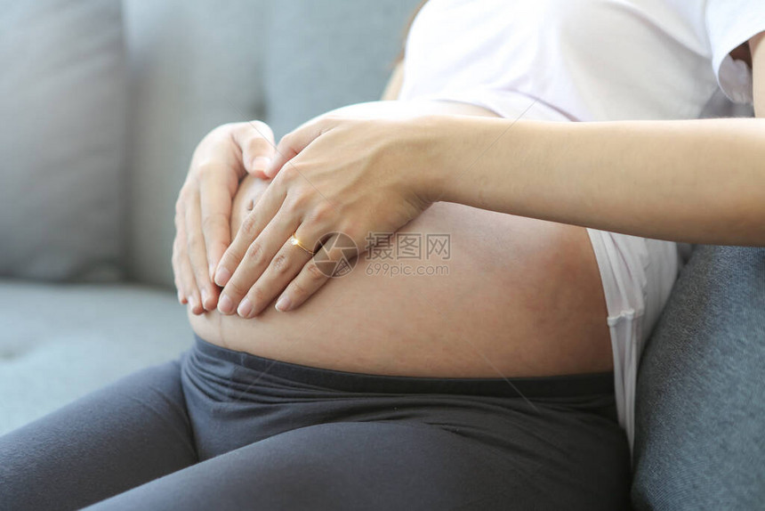 一位年轻的母亲正在她的肚子上做一只心形的手图片