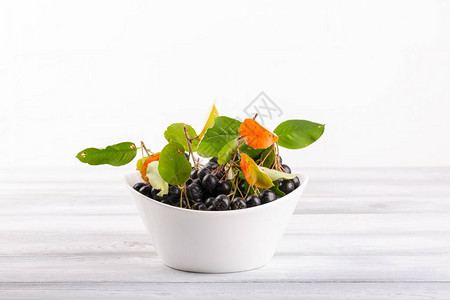 白色碗里新鲜的黑胡萝卜莓和叶子Aroniamelano图片