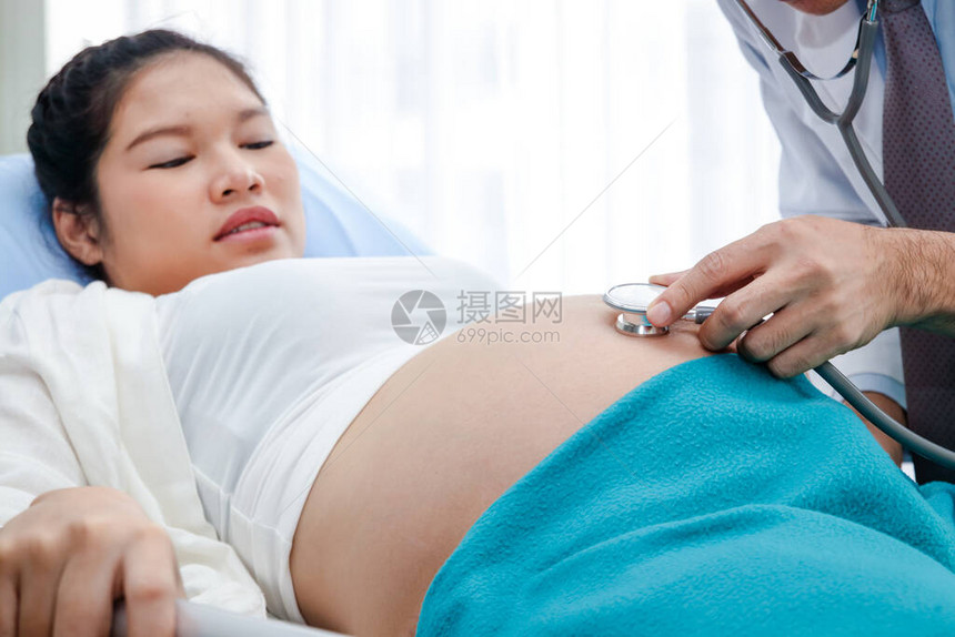 医生用钟形听诊器检查躺在诊所床上的妇女的怀孕情况图片