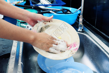 女人的手洗碗叉和勺子与水槽图片