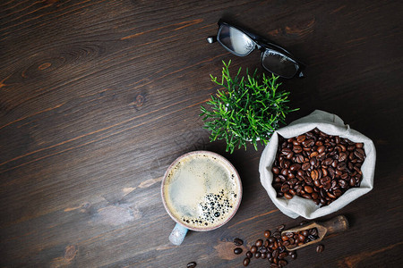 咖啡杯油布袋中的咖啡豆木桌背景上的植物和眼镜顶图片