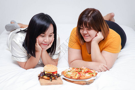 两个胖女孩在卧室的床上吃披萨和汉堡图片