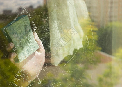 一名使用清洁海绵和橡胶手套打扫窗户的妇女擦玻璃该女孩正在对图片