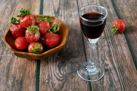手拿一杯酒上木制背景的碗里多汁新鲜美味的草莓图片