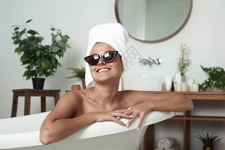 穿着毛巾和墨镜的时髦女人在家中或酒店接受温泉治疗图片