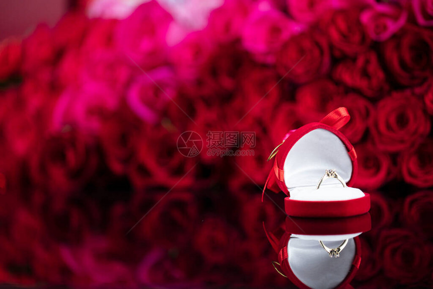 浪漫的白天概念红玫瑰背景上闪亮桌边的结婚戒指图片