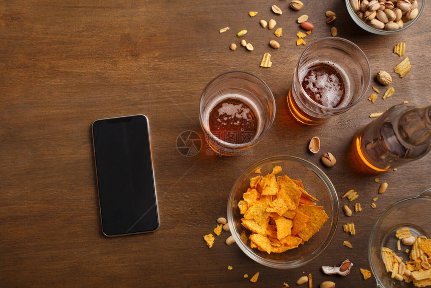 智能手机两杯啤酒瓶酒活塞和薯片都分散在桌子上图片