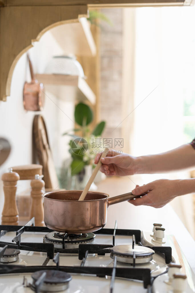 妇女站在厨房用木制室内风格现代家具和煤气炉灶上烹饪食品图片