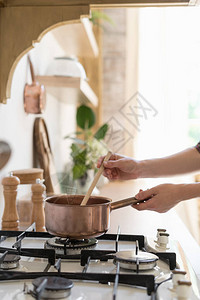 妇女站在厨房用木制室内风格现代家具和煤气炉灶上烹饪食品图片