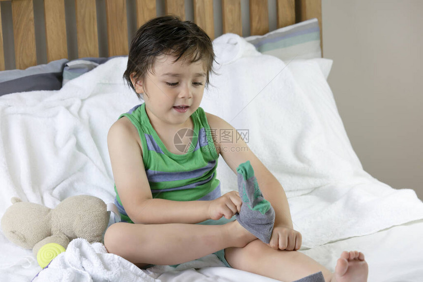 可爱的小孩坐在床上学习如何自己穿袜子的肖像图片