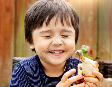 脸蛋可爱的可爱男孩的肖像喜欢在花园里吃烤鸡腿图片