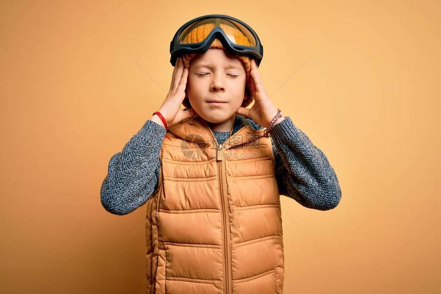 年轻的白人小孩戴着雪镜和黄色背景的冬衣图片