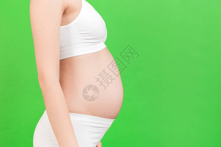 在绿色背景下关闭孕妇的腹部女孩穿着白色内衣生育概图片
