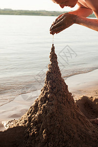 一个人建了一个沙城堡在阳光日的海滩上拍到图片