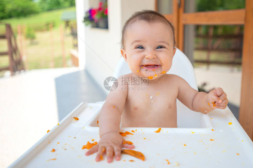 6个月的可爱又肮脏的小女婴坐在婴儿椅子上吃东西图片