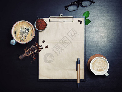 剪贴板与空白牛皮纸信笺咖啡杯烤咖啡豆笔和黑桌背景上的咖啡粉图片