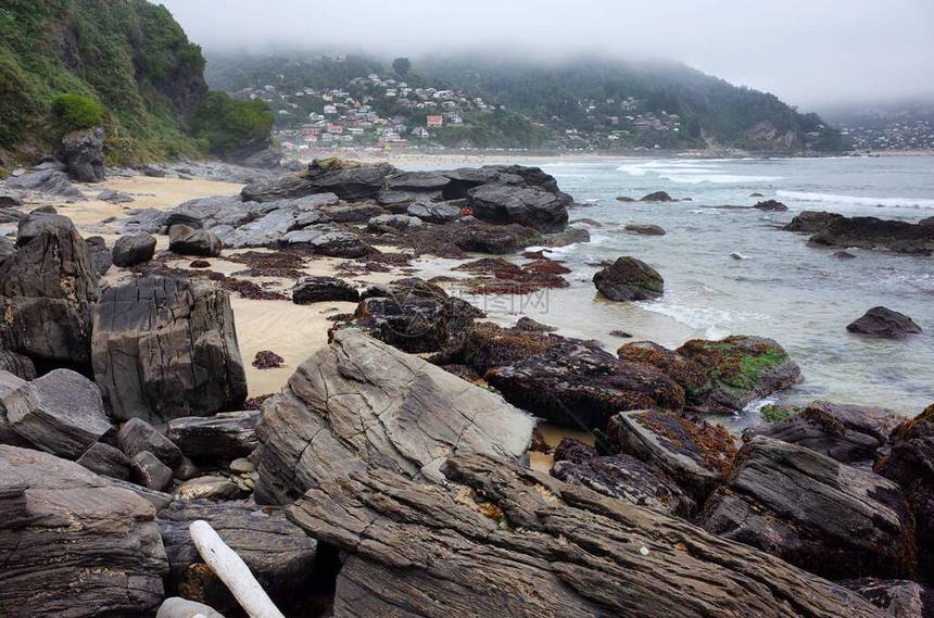 海洋滩上的巨大岩石有雾的阴天背景小山上的小村庄Maicolpue图片