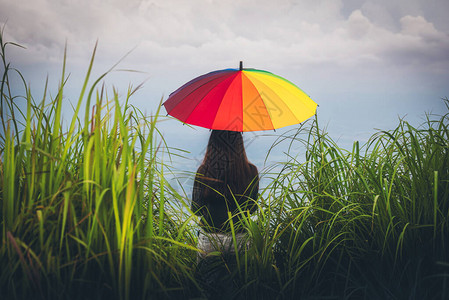 年轻女子拿着色彩多的雨伞在山上看雨图片