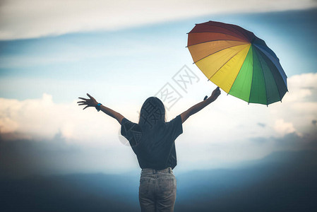 年轻女子拿着色彩多的雨伞在山上看雨图片