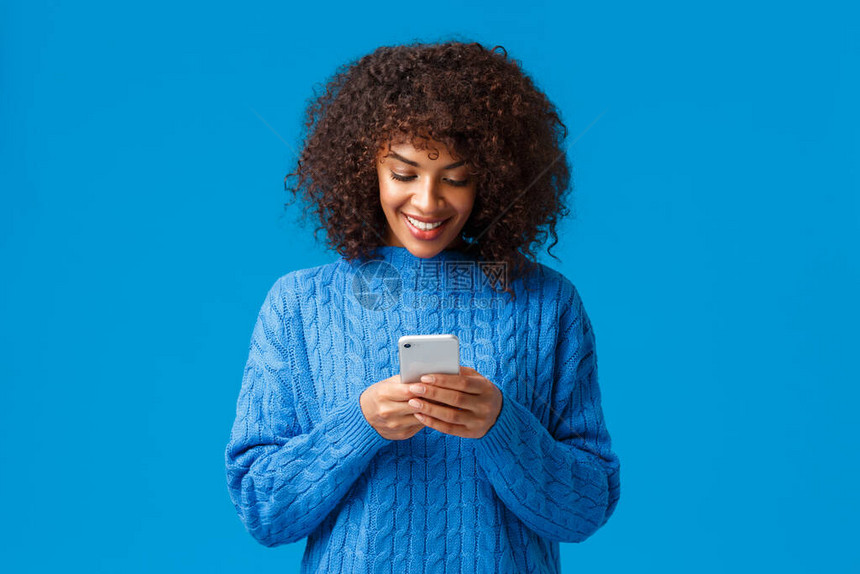 有吸引力的非裔美籍女在电话上回答男友用智能手机聊天写信息看移动屏幕和微笑穿冬季毛衣等图片